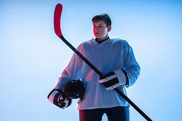 Image showing Young male hockey player with the stick on ice court and white background in neon light