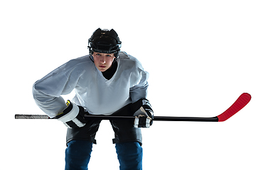 Image showing Young male hockey player with the stick on ice court and white background