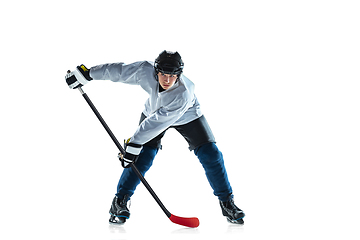 Image showing Young male hockey player with the stick on ice court and white background