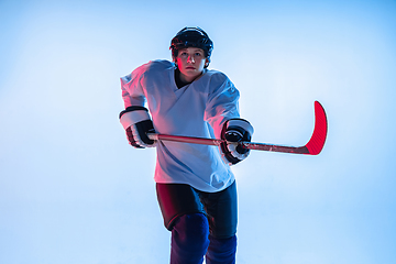 Image showing Young male hockey player with the stick on ice court and white background in neon light