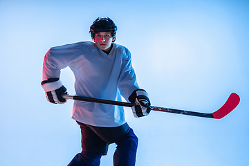 Image showing Young male hockey player with the stick on ice court and white background in neon light