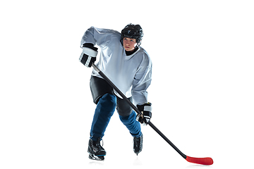 Image showing Young male hockey player with the stick on ice court and white background