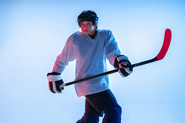 Image showing Young male hockey player with the stick on ice court and white background in neon light