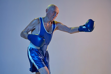 Image showing Senior man wearing sportwear boxing isolated on gradient studio background in neon light. Concept of sport, activity, movement, wellbeing. Copyspace, ad.