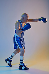 Image showing Senior man wearing sportwear boxing isolated on gradient studio background in neon light. Concept of sport, activity, movement, wellbeing. Copyspace, ad.