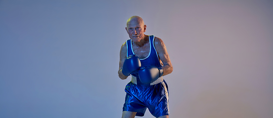 Image showing Senior man wearing sportwear boxing isolated on gradient studio background in neon light. Concept of sport, activity, movement, wellbeing. Copyspace, ad.