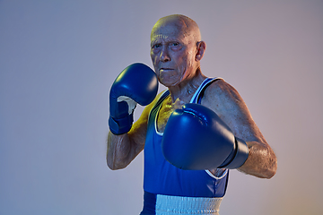 Image showing Senior man wearing sportwear boxing isolated on gradient studio background in neon light. Concept of sport, activity, movement, wellbeing. Copyspace, ad.