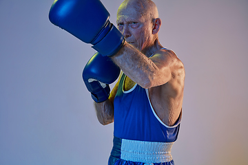 Image showing Senior man wearing sportwear boxing isolated on gradient studio background in neon light. Concept of sport, activity, movement, wellbeing. Copyspace, ad.