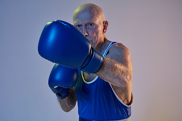 Image showing Senior man wearing sportwear boxing isolated on gradient studio background in neon light. Concept of sport, activity, movement, wellbeing. Copyspace, ad.