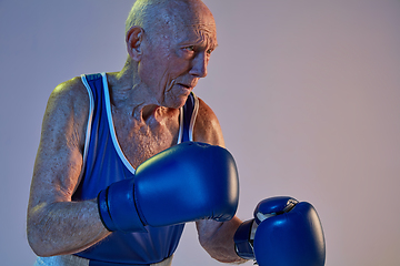 Image showing Senior man wearing sportwear boxing isolated on gradient studio background in neon light. Concept of sport, activity, movement, wellbeing. Copyspace, ad.