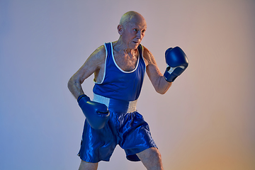 Image showing Senior man wearing sportwear boxing isolated on gradient studio background in neon light. Concept of sport, activity, movement, wellbeing. Copyspace, ad.