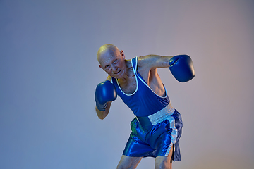 Image showing Senior man wearing sportwear boxing isolated on gradient studio background in neon light. Concept of sport, activity, movement, wellbeing. Copyspace, ad.