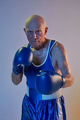 Image showing Senior man wearing sportwear boxing isolated on gradient studio background in neon light. Concept of sport, activity, movement, wellbeing. Copyspace, ad.