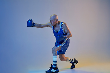 Image showing Senior man wearing sportwear boxing isolated on gradient studio background in neon light. Concept of sport, activity, movement, wellbeing. Copyspace, ad.