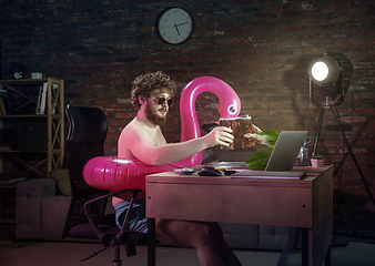 Image showing Young man drinking beer during online meeting with friends on video call.