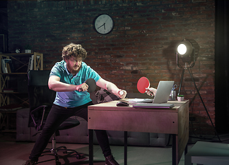 Image showing Young Caucasian man playing tennis with friend online through laptop at home.