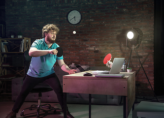 Image showing Young Caucasian man playing tennis with friend online through laptop at home.