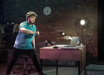 Image showing Young Caucasian man playing tennis with friend online through laptop at home.