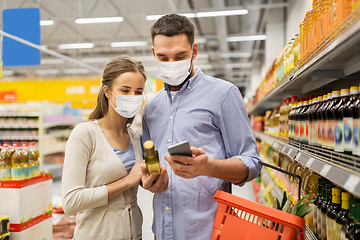 Image showing couple in masks with phone and olive oil at store