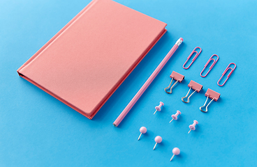 Image showing pink notebook, pins, clips and pencil on blue