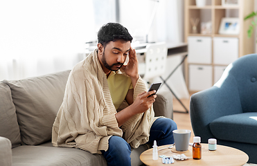 Image showing sick young man in blanket with smartphone at home