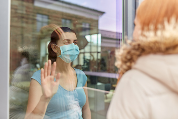 Image showing ill woman in mask looking at friend through window