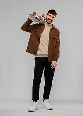 Image showing smiling young man in brown jacket with skateboard