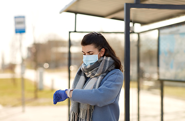 Image showing woman in mask looking at wristwatch at bus stop