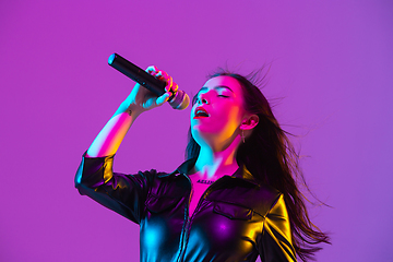 Image showing Caucasian female singer portrait isolated on purple studio background in neon light