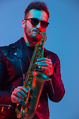 Image showing Young caucasian jazz musician playing the saxophone in neon light