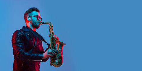 Image showing Young caucasian jazz musician playing the saxophone in neon light, flyer