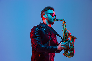 Image showing Young caucasian jazz musician playing the saxophone in neon light