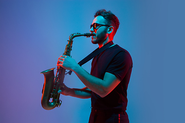 Image showing Young caucasian jazz musician playing the saxophone in neon light