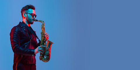 Image showing Young caucasian jazz musician playing the saxophone in neon light, flyer