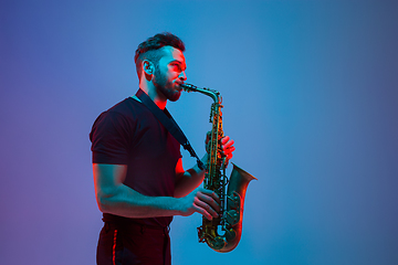 Image showing Young caucasian jazz musician playing the saxophone in neon light