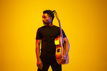 Image showing Young african-american musician singing, playing guitar in neon light