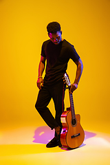 Image showing Young african-american musician singing, playing guitar in neon light