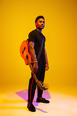 Image showing Young african-american musician singing, playing guitar in neon light