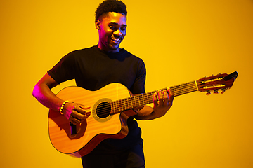 Image showing Young african-american musician singing, playing guitar in neon light