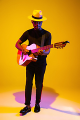 Image showing Young african-american musician singing, playing guitar in neon light