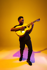 Image showing Young african-american musician singing, playing guitar in neon light