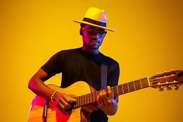 Image showing Young african-american musician singing, playing guitar in neon light