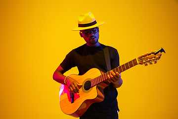 Image showing Young african-american musician singing, playing guitar in neon light