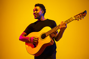 Image showing Young african-american musician singing, playing guitar in neon light