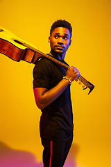 Image showing Young african-american musician singing, playing guitar in neon light