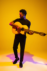 Image showing Young african-american musician singing, playing guitar in neon light