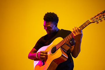 Image showing Young african-american musician singing, playing guitar in neon light