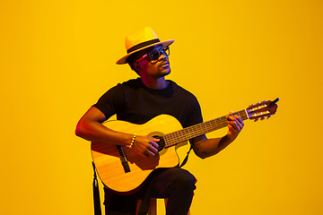 Image showing Young african-american musician singing, playing guitar in neon light