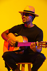 Image showing Young african-american musician singing, playing guitar in neon light