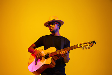 Image showing Young african-american musician singing, playing guitar in neon light